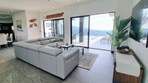 Un salon moderne avec un canapé d’angle, une table basse et une grande fenêtre donnant sur l’extérieur.