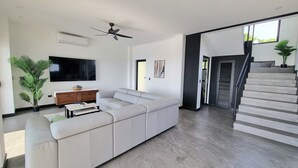 Un salon moderne avec un canapé d’angle, un téléviseur à écran plat, un ventilateur de plafond et un escalier.
