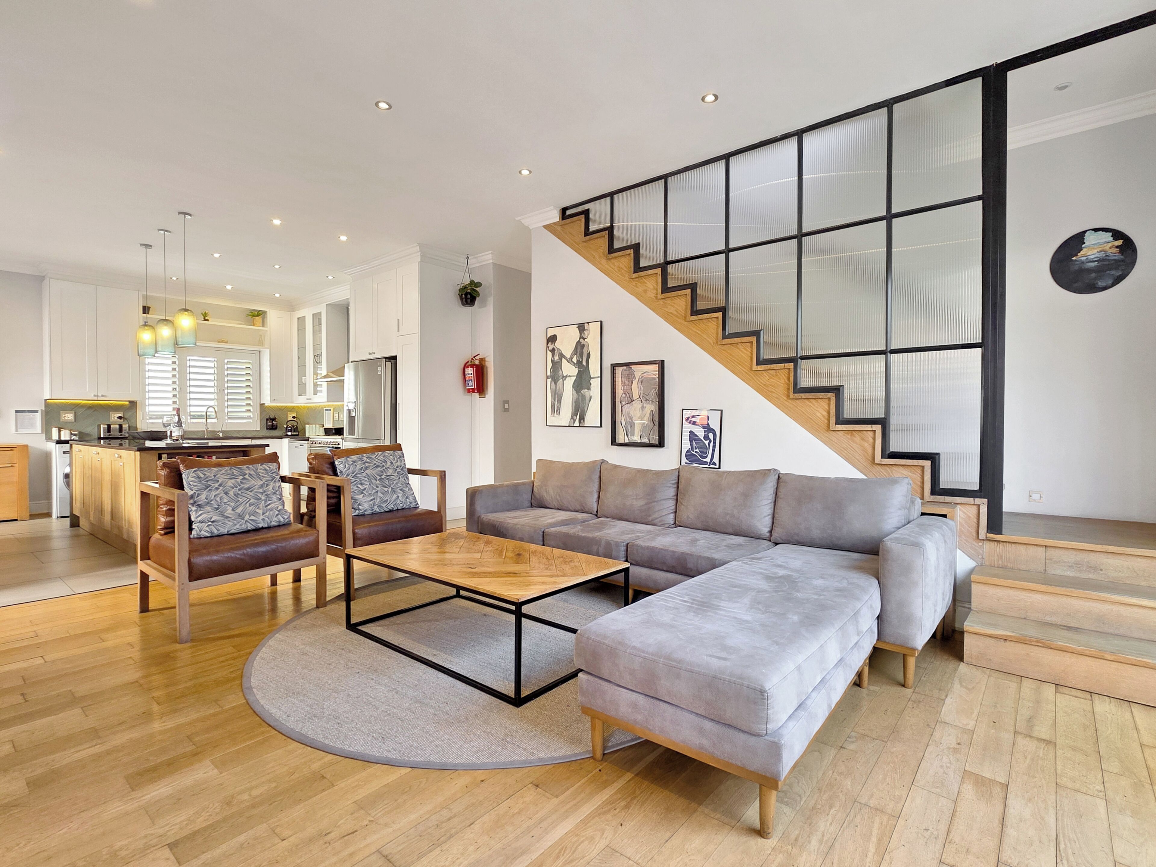 A modern living room with a sectional sofa, a wooden coffee table, and a staircase with glass railings.