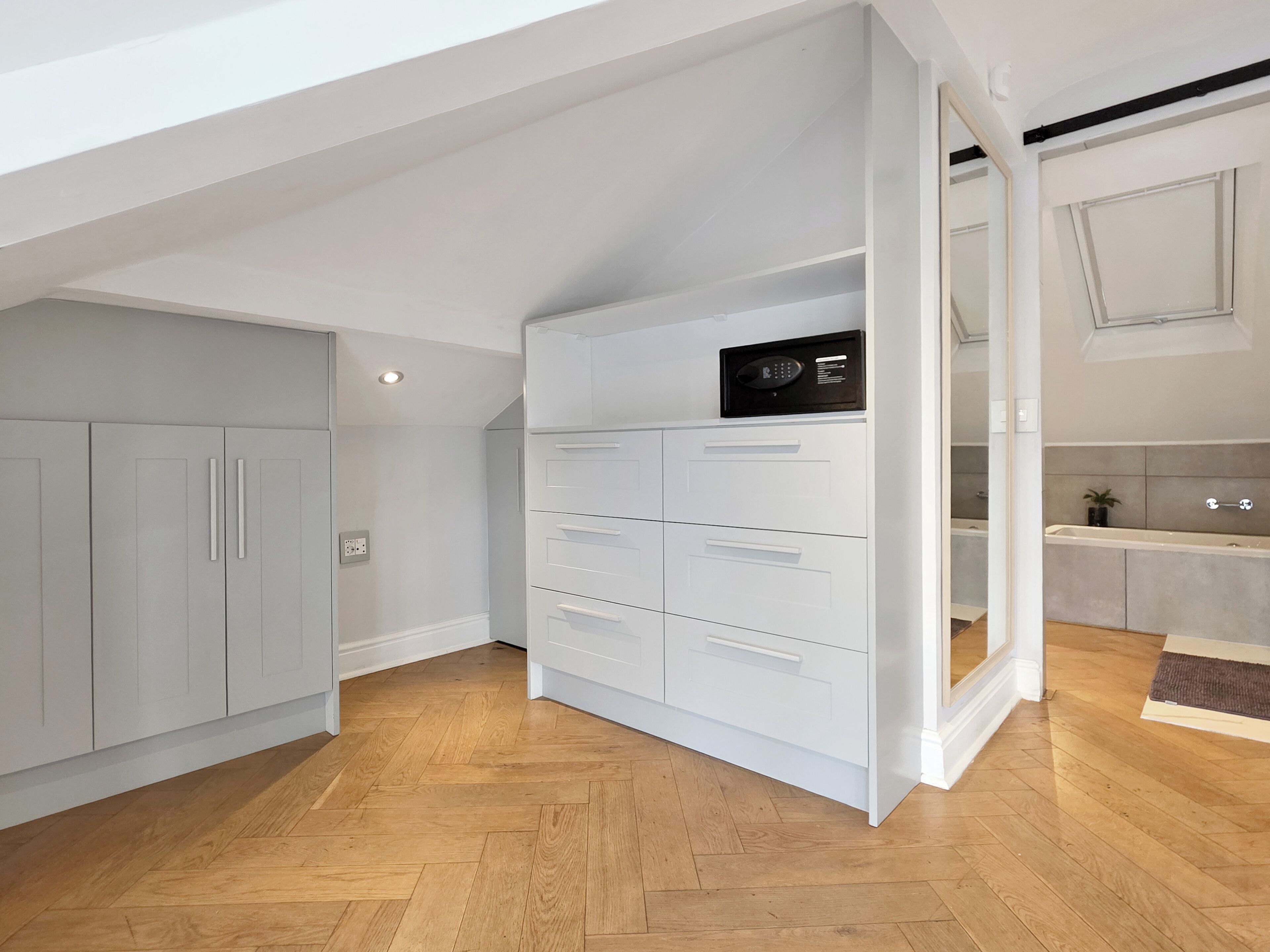 A modern kitchen with white cabinetry, a built-in oven, and a wooden herringbone floor.