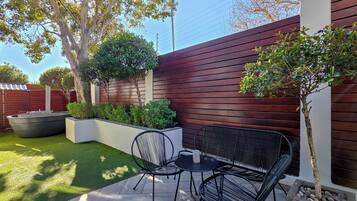 An outdoor patio with a table and chairs, surrounded by a wooden fence and greenery.
