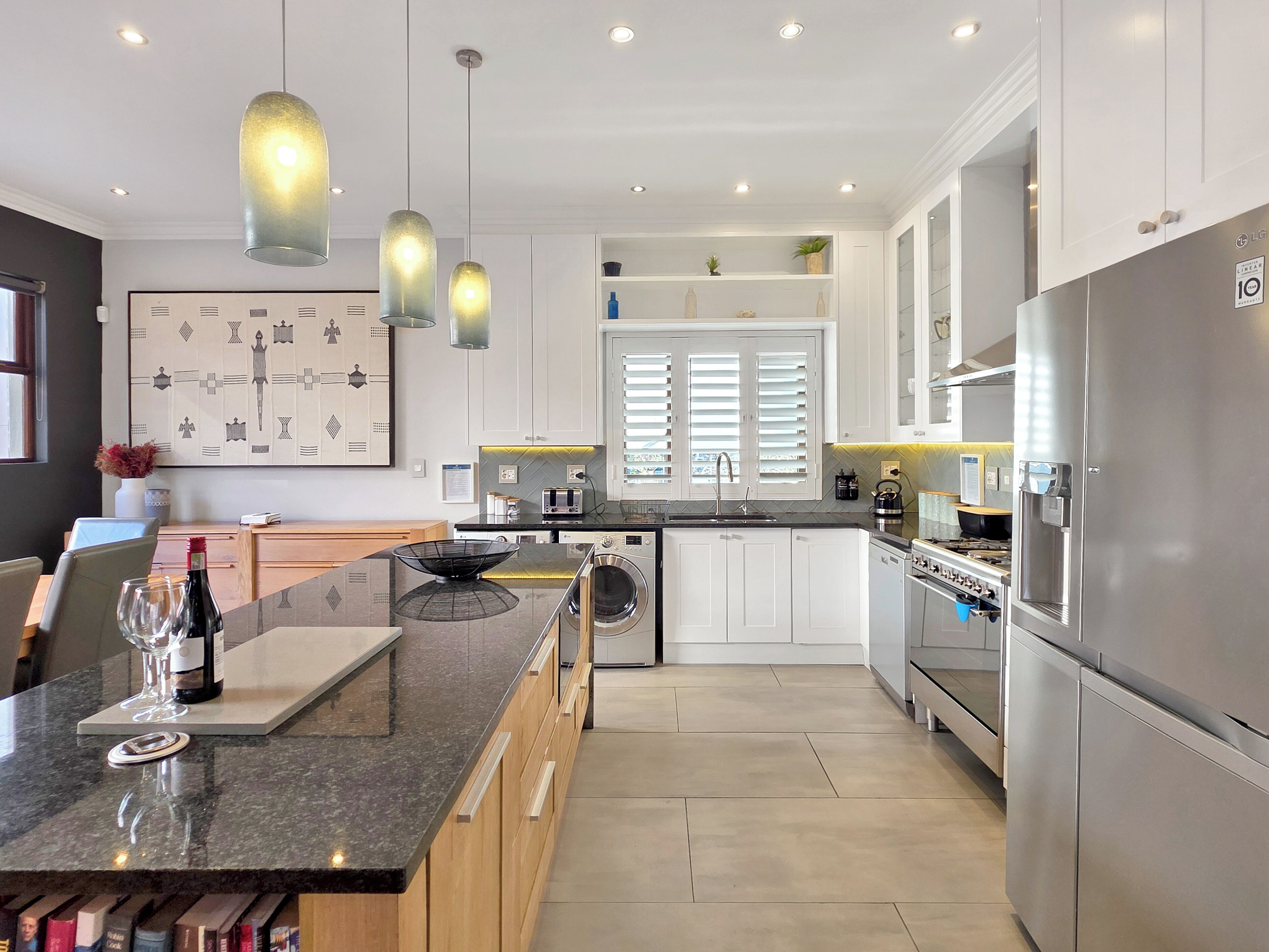 A modern kitchen with stainless steel appliances, a granite countertop, pendant lighting, and a view of the dining area.