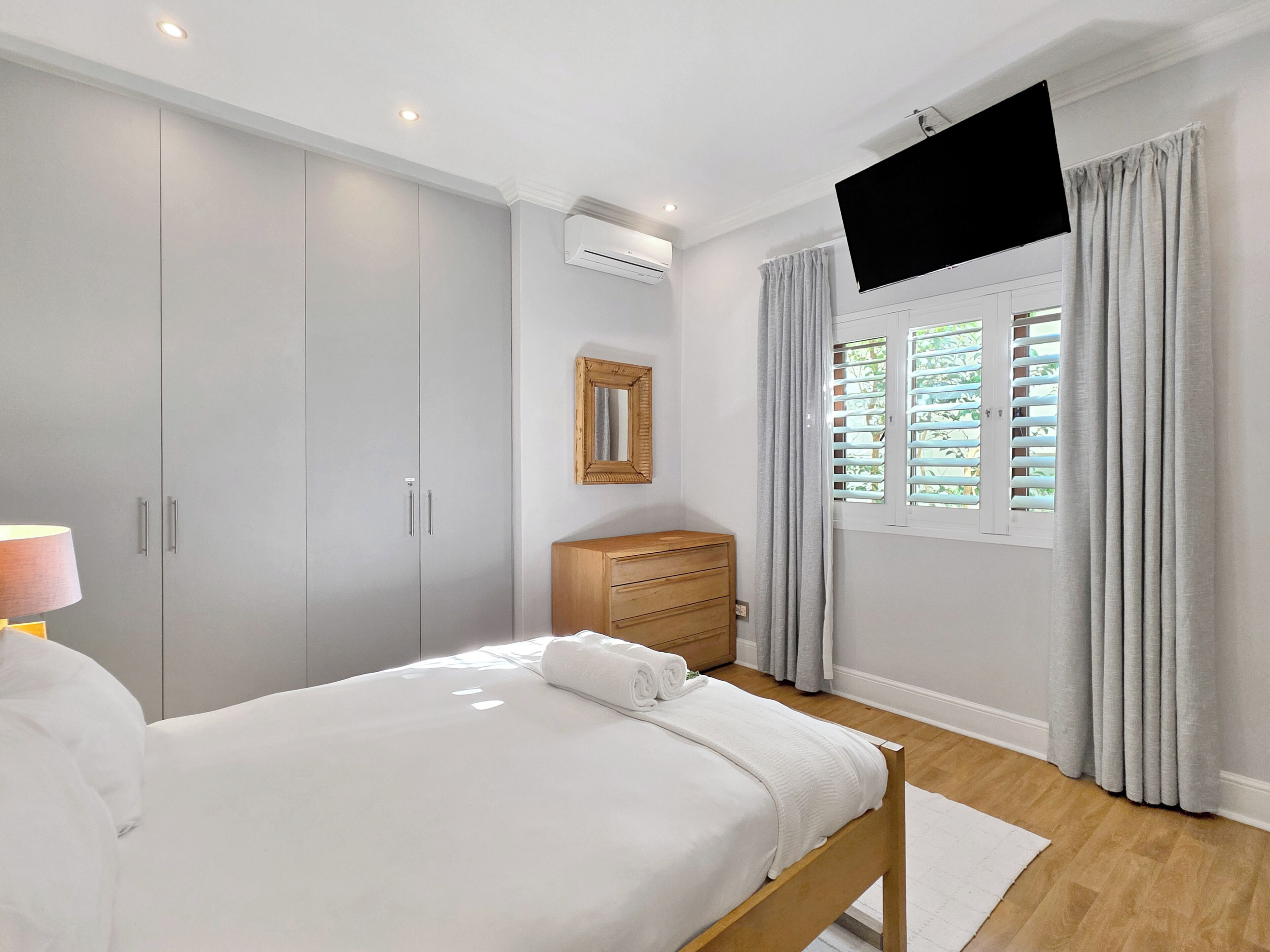 A bedroom with a bed, wardrobe, mirror, TV, and window with curtains.