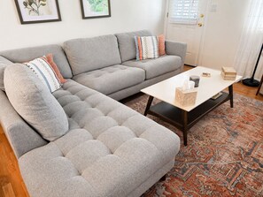 Ein Wohnzimmer mit einem grauen Ecksofa, einem weißen Couchtisch und einem gemusterten Teppich.