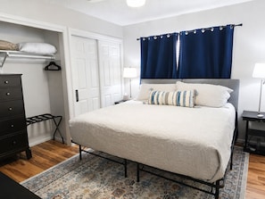 Ein Schlafzimmer mit Bett, Kommode, Tür, Nachttisch und Lampe.