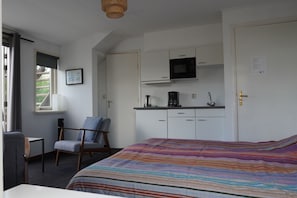 Ein Schlafzimmer mit Bett, Stuhl, Schreibtisch, einer Küchenzeile und einem Fenster.