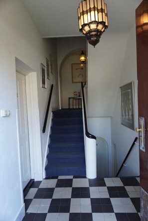 Una escalera con piso a cuadros, un rellano cubierto de alfombra azul y un aplique en la pared.