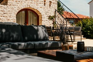 Un edificio de piedra con un amplio arco de entrada, mobiliario exterior con un sofá y sillones, y una planta en maceta.