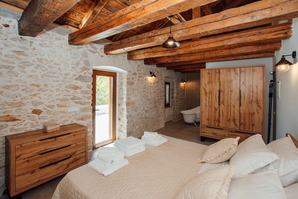 Un dormitorio con paredes de piedra, vigas de madera, una cama con ropa de cama blanca, un aparador de madera y un armario de madera.