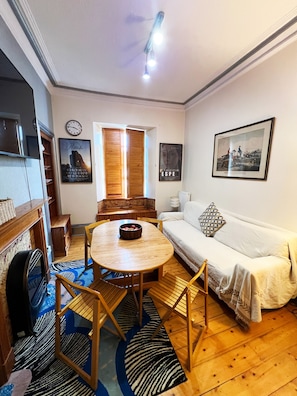 A living room with a round wooden table, a sofa, a clock, and a framed picture on the wall. - Flat, Arthur Seat view, walking distance to Castle (Edinburgh)