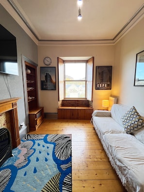 A cozy room with a wooden bench, a white sofa, a patterned rug, a fireplace, and a window with a view. - Flat, Arthur Seat view, walking distance to Castle (Edinburgh)