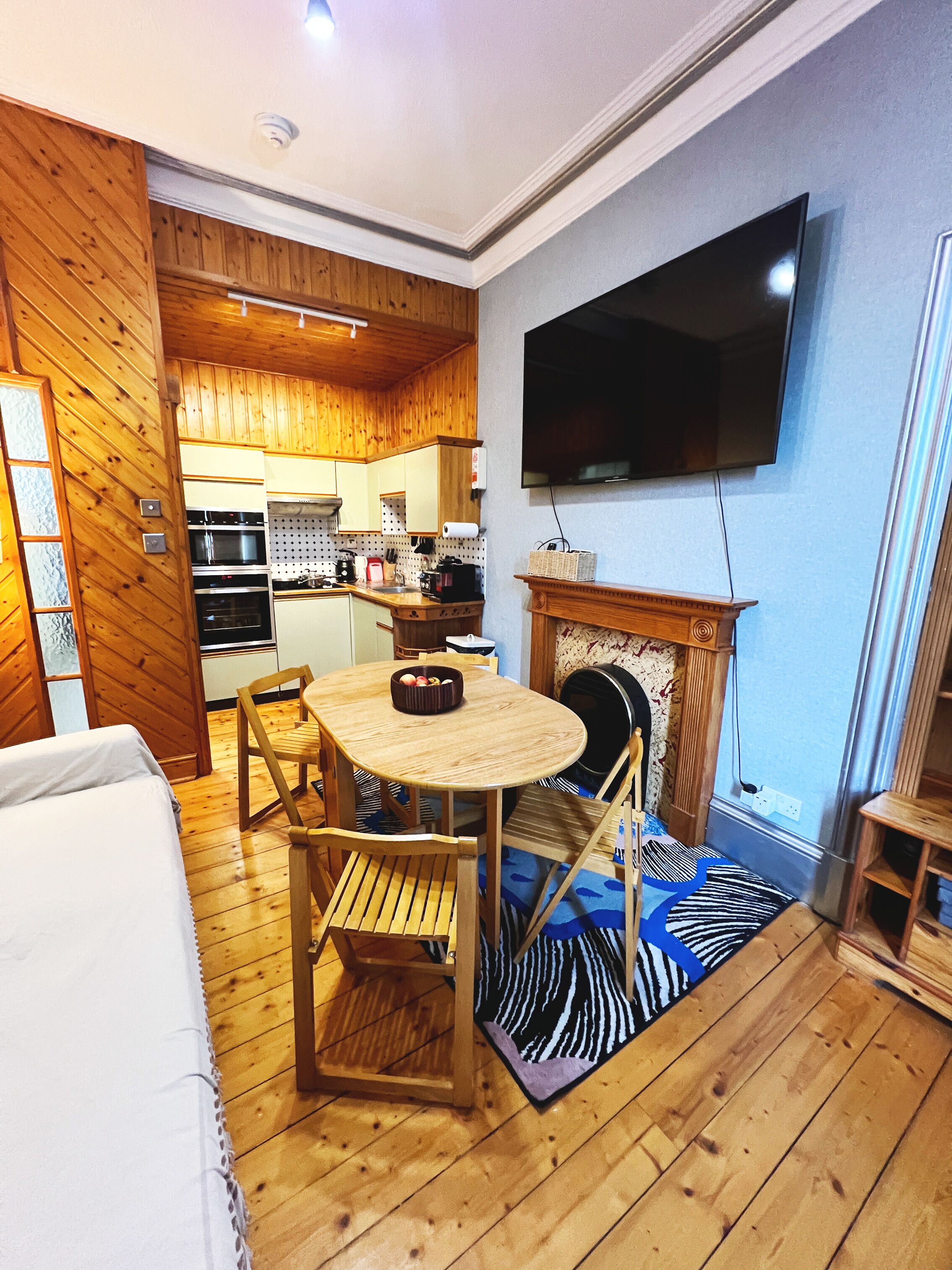 Un salon au plancher de bois, avec une table à manger, des chaises, un téléviseur à écran plat fixé au mur et une cheminée.