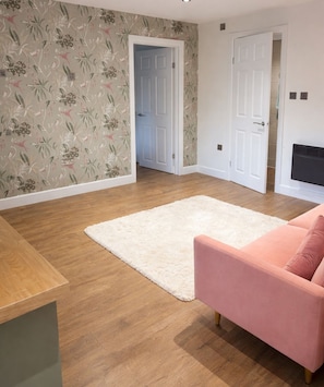 Ein Wohnzimmer mit Holzboden, einem weißen Teppich, einem rosa Sofa und blumigem Wandpapier.
