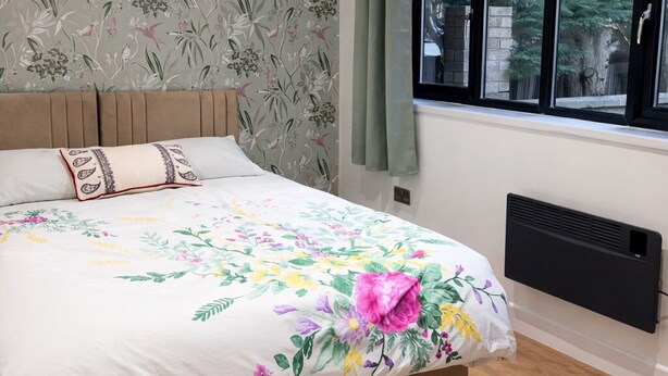 A bedroom with a bed, floral wallpaper, a window, and a radiator. - Spacious 2-BR Annexe near Abington Park - 10% off (West Northamptonshire)