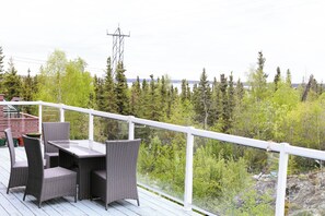 A deck with wicker furniture and a railing overlooking a forested area. - Charming Retreat with Stunning Views in Yellowknife's Prestigious Neighborhood (Yellowknife)