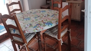 A dining area with a table set for four, surrounded by wooden chairs. A television is mounted on the wall above the table. - Les Orangers Vacation Rental (Pleubian)