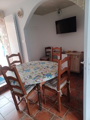 Ein Essbereich mit einem Tisch, gedeckt für vier Personen, umgeben von Holzsesseln. Über dem Tisch ist ein Fernseher an der Wand montiert.