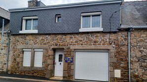 A two-story stone building with a garage door, two windows with shutters, and a stone facade. - Les Orangers Vacation Rental (Pleubian)