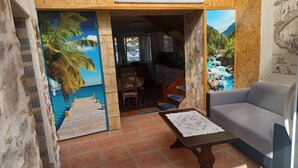 A room with a view of a tropical beach, a dining area with a table and chairs, and a sofa. - Les Orangers Vacation Rental (Pleubian)