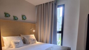 A hotel room with a bed, curtains, a window, and a wall-mounted light fixture. - F.206 | Your Refuge with comfort and good taste (Tamandaré)