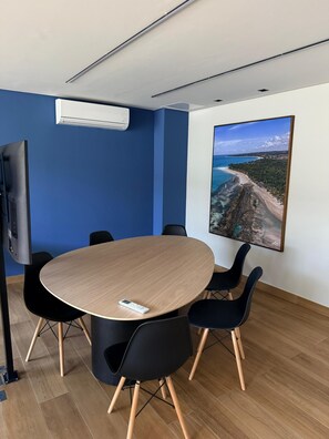 Ein Konferenzraum mit rundem Tisch, schwarzen Stühlen, einem angebrachten Fernseher und großformatiger Wandkunst.