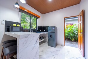 A kitchen with a marble countertop, a refrigerator, a microwave, and a window with a view of greenery. - River Collection - Villa Essence #4 cabin in beautiful La Fortuna (La Fortuna)