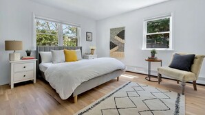 Une chambre à coucher avec un lit, des tables de chevet, une chaise, un tapis et de grandes fenêtres.