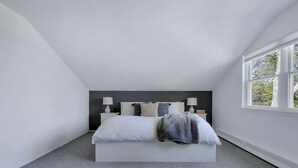 A bedroom with a large bed, two bedside tables with lamps, a window with a view of trees, and a grey carpet.