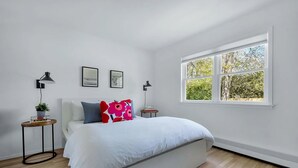 A bedroom with a bed, two bedside tables, a window, and a view of trees.