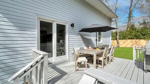A deck with a table and chairs, a grill, and a sliding glass door leading to an interior space.