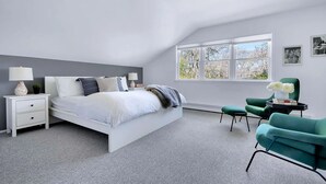 Une chambre à coucher avec un lit, des tables de chevet, une chaise, une fenêtre et une vue sur les arbres.