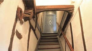 Uma escadaria estreita com corrimãos de madeira e uma porta no topo.