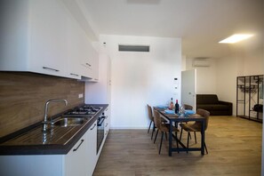 Une cuisine compacte équipée d’une cuisinière, d’un évier et d’un plan de travail en bois, qui donne sur un coin repas avec une table dressée pour quatre personnes.