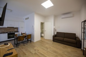 Ein kompakter Wohnbereich mit Küchenzeile, Essplatz, Sofa und einer Tür zu einem weiteren Zimmer.
