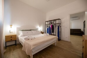 Une chambre à coucher comprenant un lit, des tables de chevet, une armoire et un couloir menant à un espace de vie.
