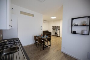 Eine kleine Küche mit Gasherd, einem Esstisch mit Stühlen, einer Couch und einer eingebauten Regaleinheit.