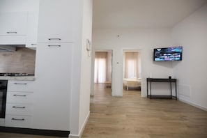 Eine moderne Wohnung mit Küche, Essbereich, Wohnzimmer mit Fernseher und Schlafzimmer mit Bett und Vorhängen.