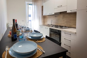 Eine moderne Küche mit weißen Schränken, einem eingebauten Backofen und einem Essbereich mit einem langen Tisch, der für eine Mahlzeit gedeckt ist.