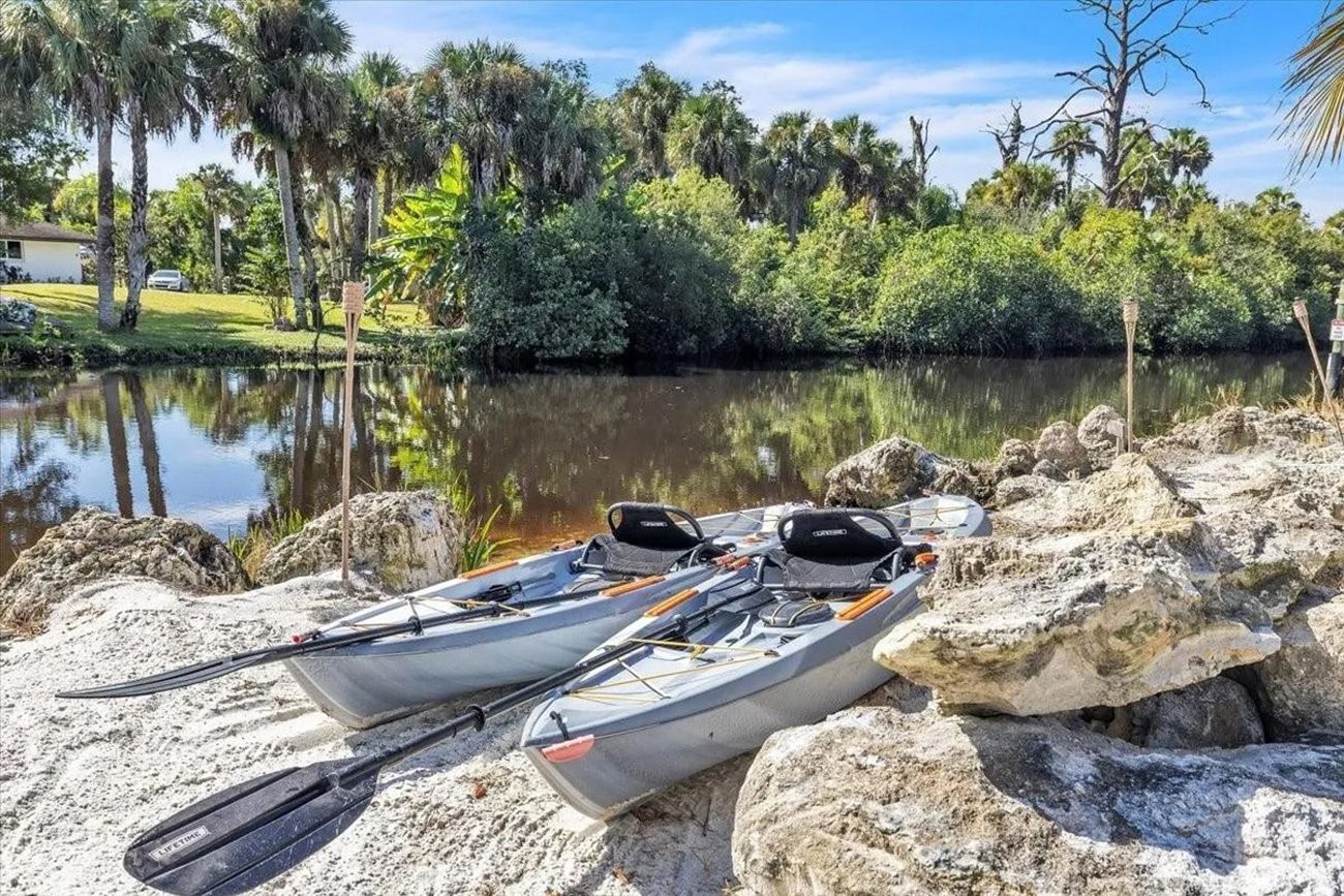 Two kayaks on a sandy shore with a calm water body and dense greenery in the background.