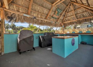 A covered outdoor area with a thatched roof, a bar counter, and covered seating.