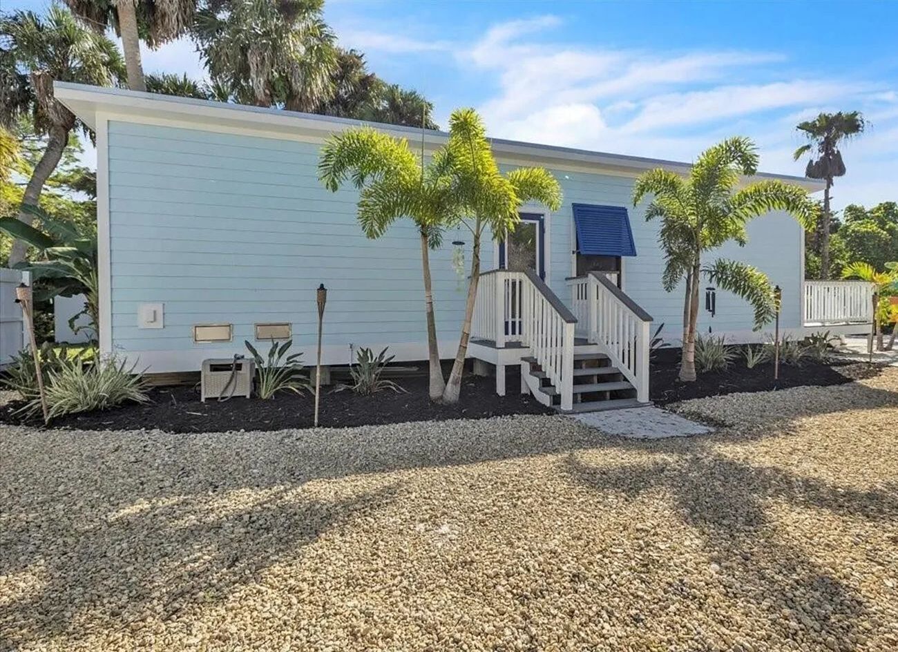 Light blue exterior home entrance with palm trees and a gravel yard.
