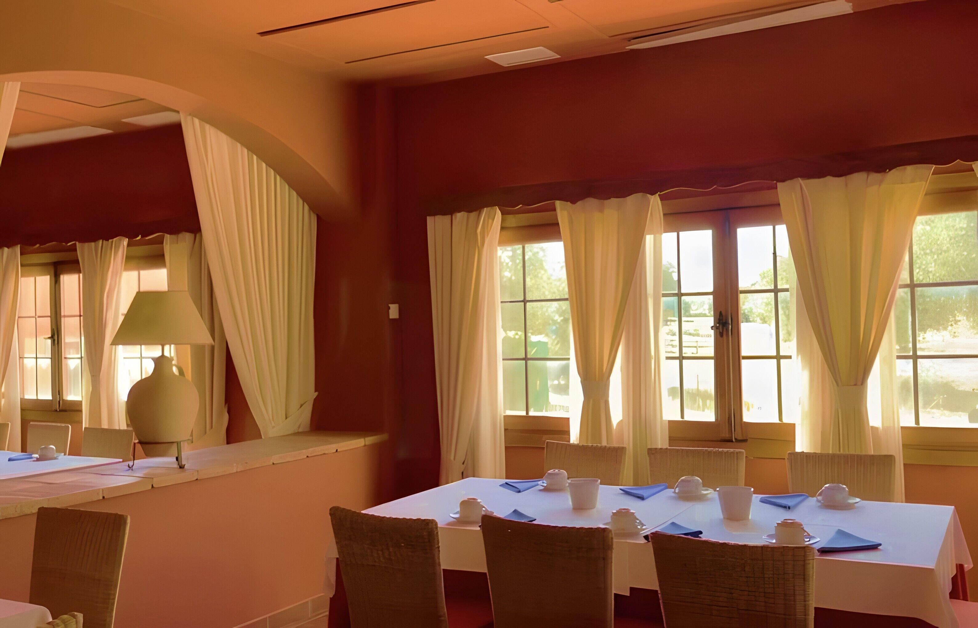 A dining area with a table set for four, chairs, a lamp, and large windows with curtains.