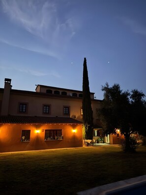 A building with a tiled roof, a tall cypress tree, and a well-lit entrance. - Private Country House with Gredos Views (Calzada de Oropesa)