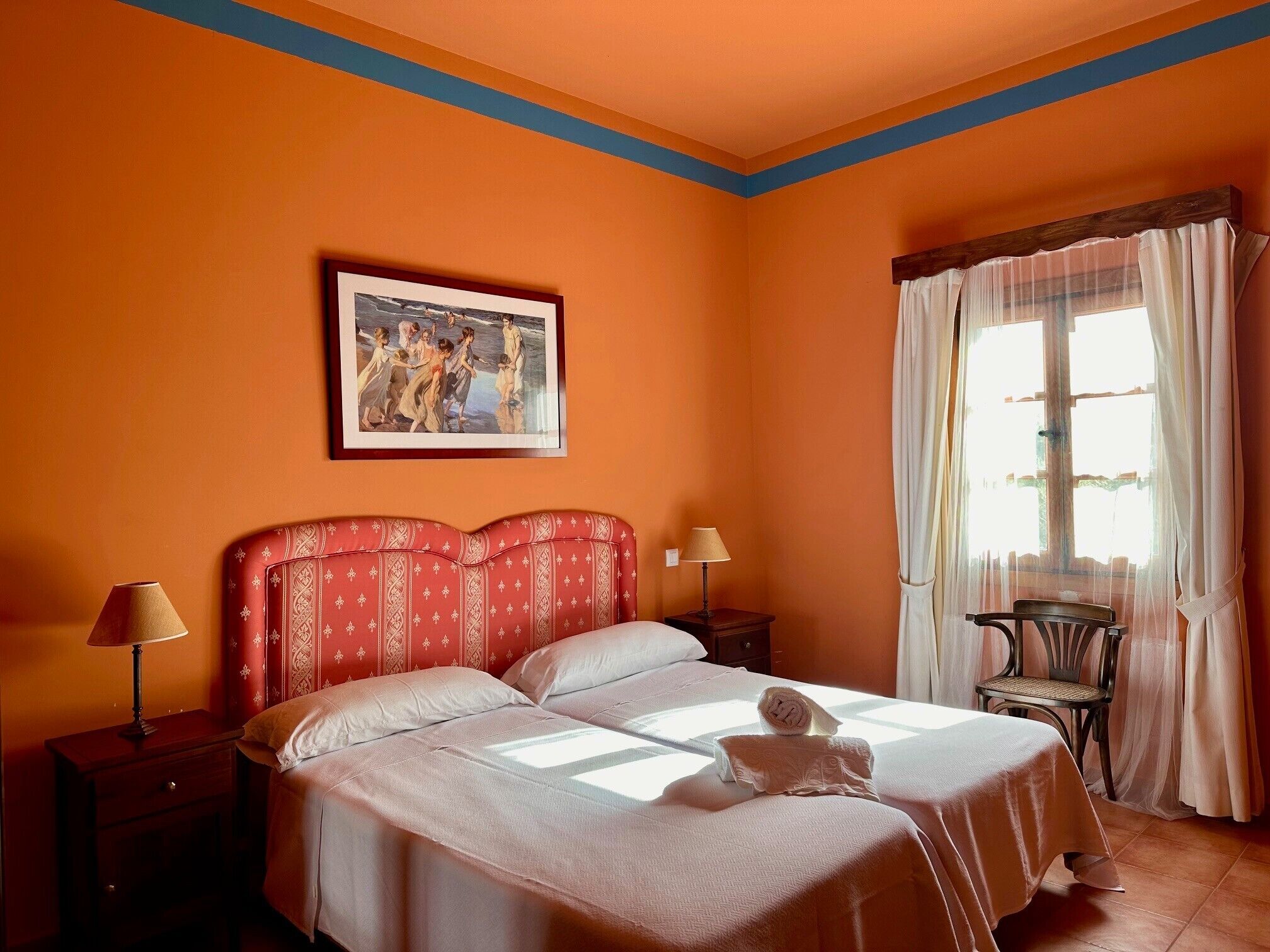 Een hotelkamer met een bed, twee nachtkastjes, een lamp, een stoel en een raam met gordijnen.