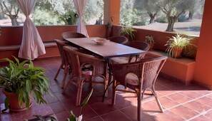 A covered patio with a table and chairs, potted plants, and a view of trees.
