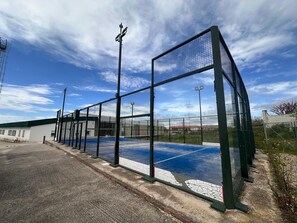A sports facility with a tennis court, surrounded by a metal fence and a building with a green roof. - Private Country House with Gredos Views (Calzada de Oropesa)