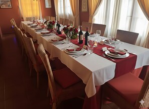 Un lungo tavolo da pranzo imbandito con tovaglioli rossi, bicchieri da vino e piatti, circondato da sedie in vimini.