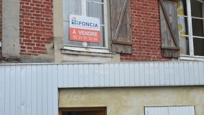 A building with a brick facade, a window with a sign advertising 'FONCIA À VENDRE,' and a door.