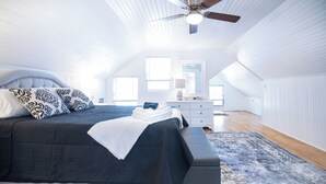 Et soveværelse med seng, natbord, lampe og en loftsvifte.