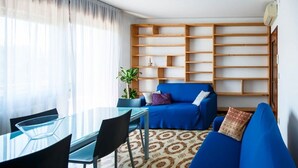 En moderne stue med et glasbord, blå sofa og en reol i træ.